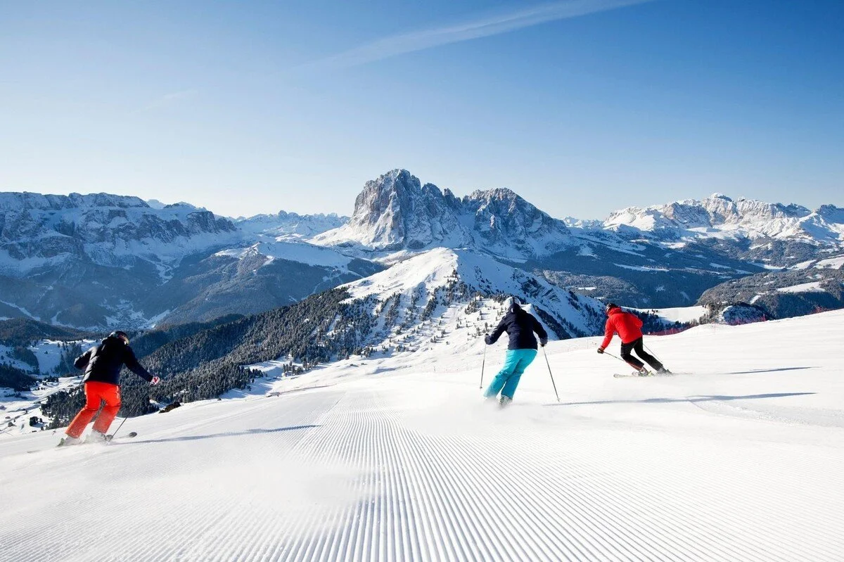 Three people skiing down a snow-covered slope with a mountainous landscape in the background.