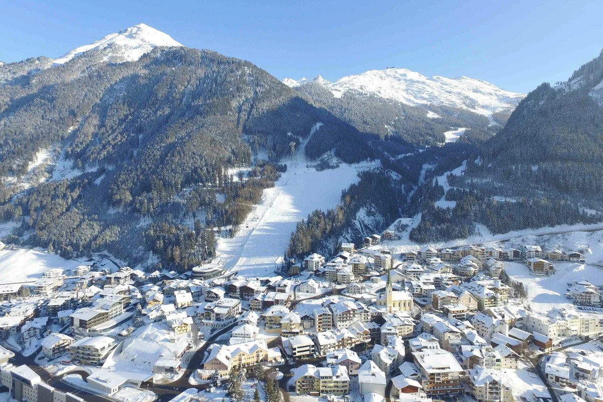 Snow-covered Ischgl town nestled among mountains with dense forest and snow-covered slopes.