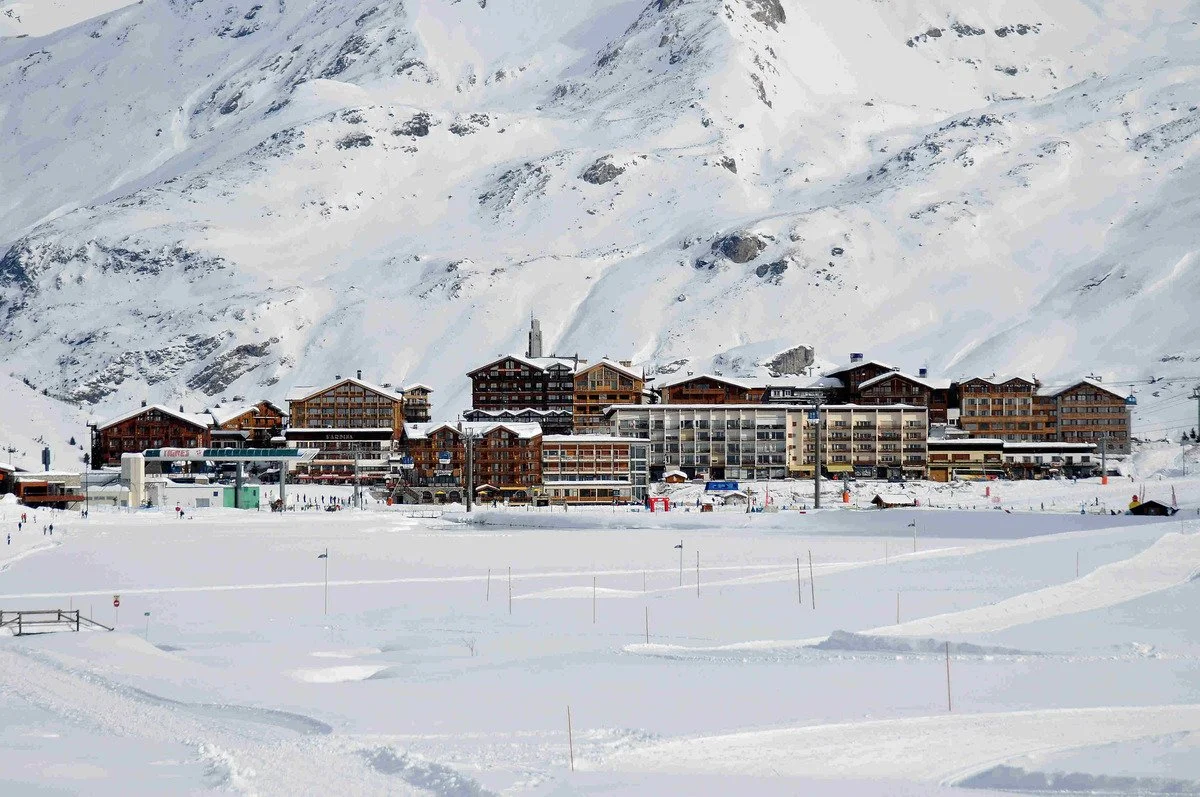 A snowy Tignes resort village with multi-story wooden buildings and ski lifts in the foreground.
