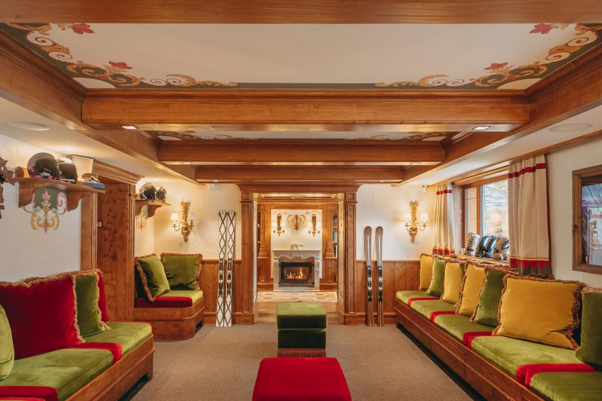 A cozy living room with wooden accents, a fireplace, green and red cushioned seating, and ski equipment near the fireplace.