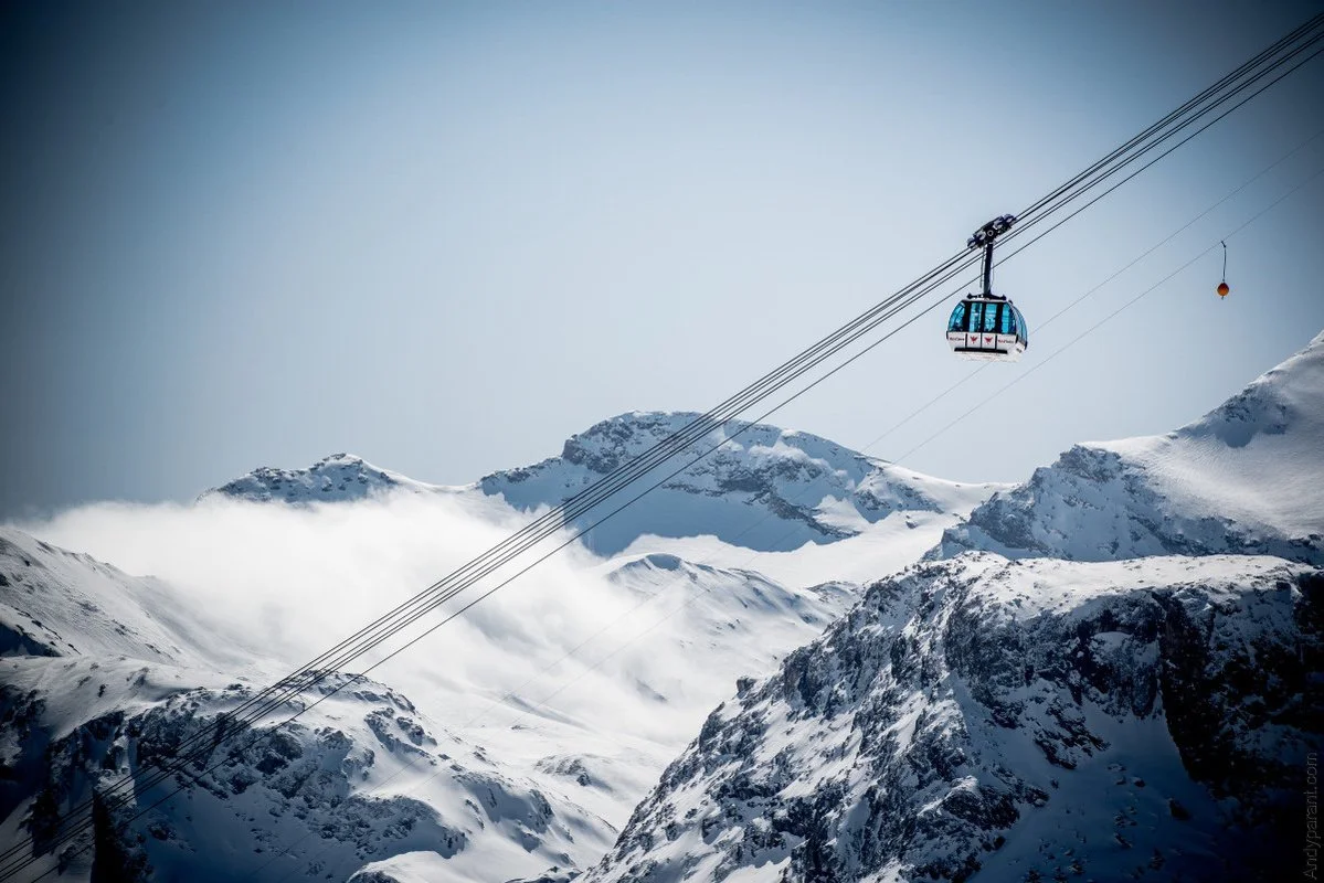 A cable car traveling above snowy mountain peaks in Val d'Isere on a clear day.