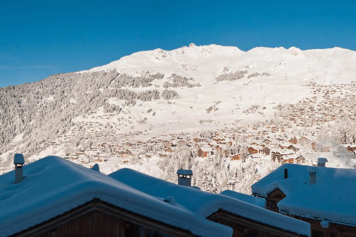 Snow-covered rooftops in Verbier with a mountain in the background under a clear blue sky.