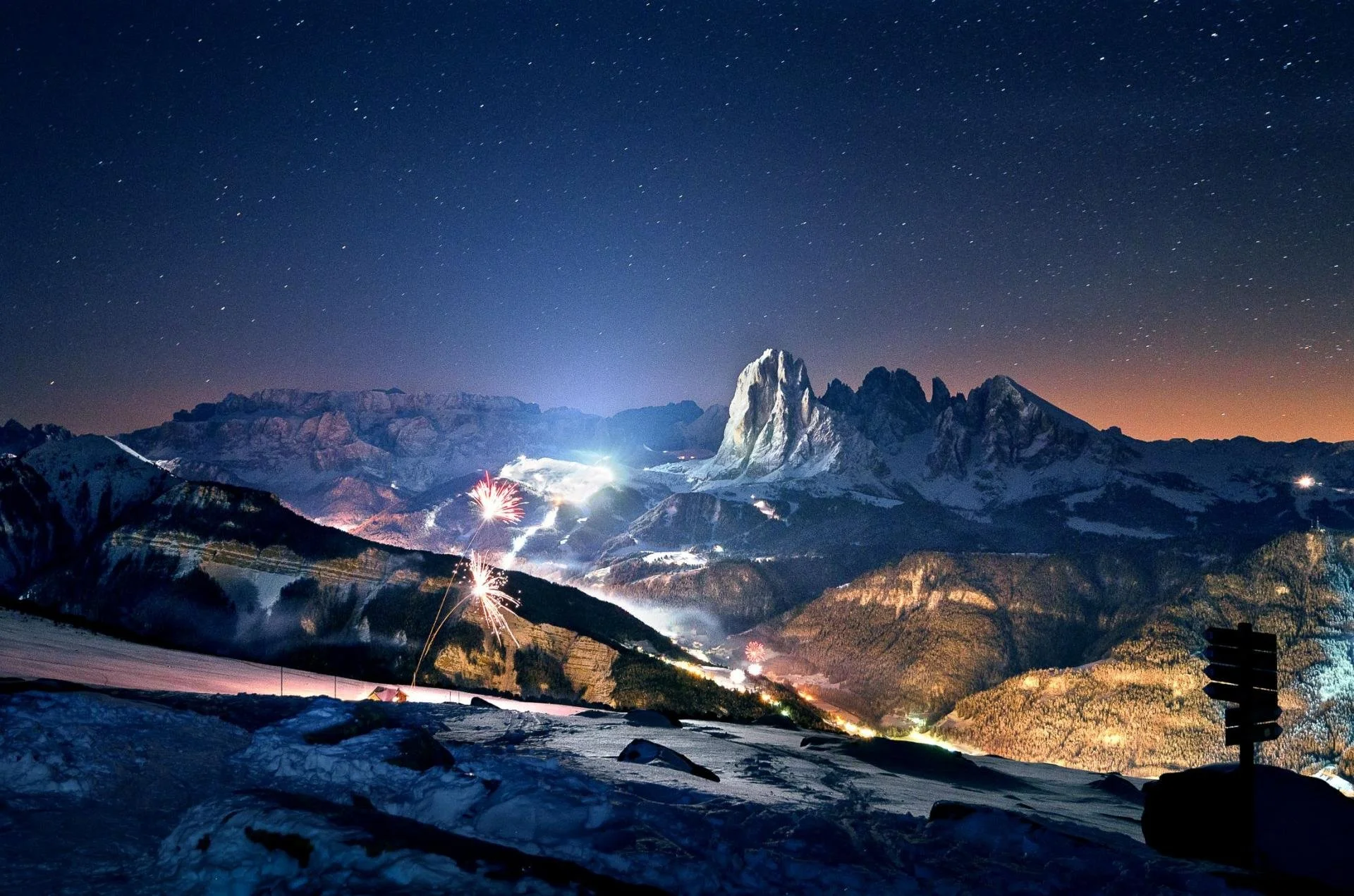 Nighttime mountain scene with fireworks, smoke, and light effects across a snowy landscape.