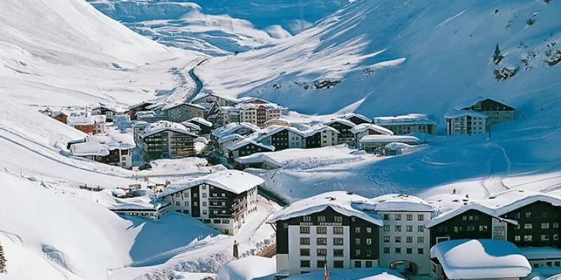 Snow-covered Zurs mountainside village with multi-story buildings and ski tracks.