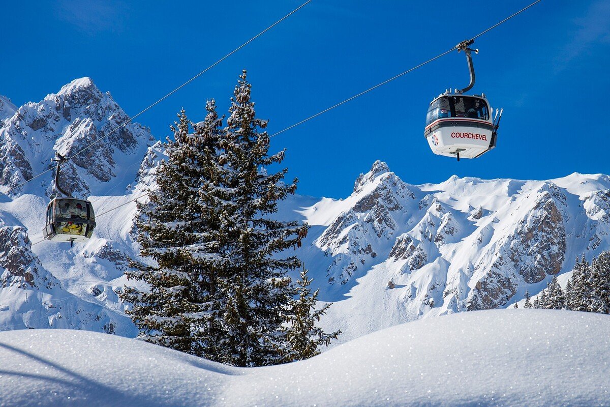 Snow-covered mountain landscape with Courchevel gondolas flying above trees in winter.