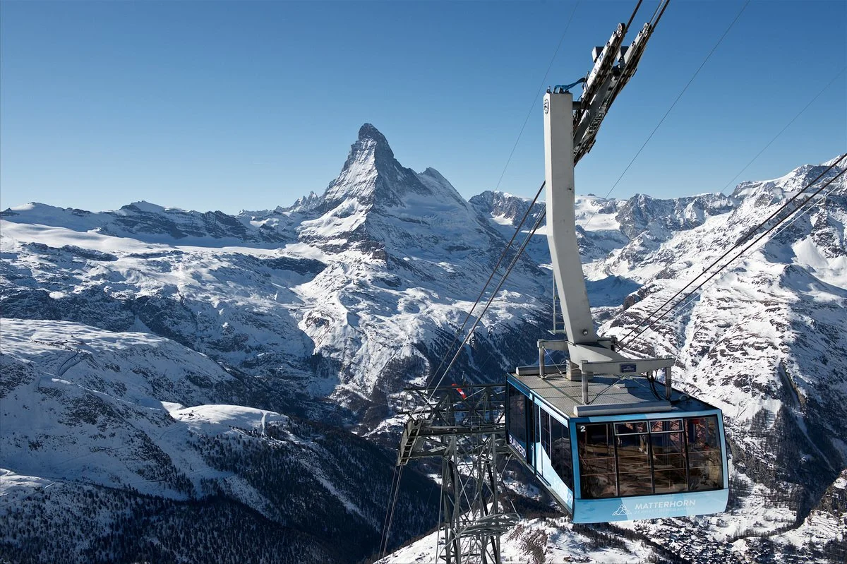 A cable car traveling over snow-covered mountains in Zermatt with the Matterhorn mountain in the background.