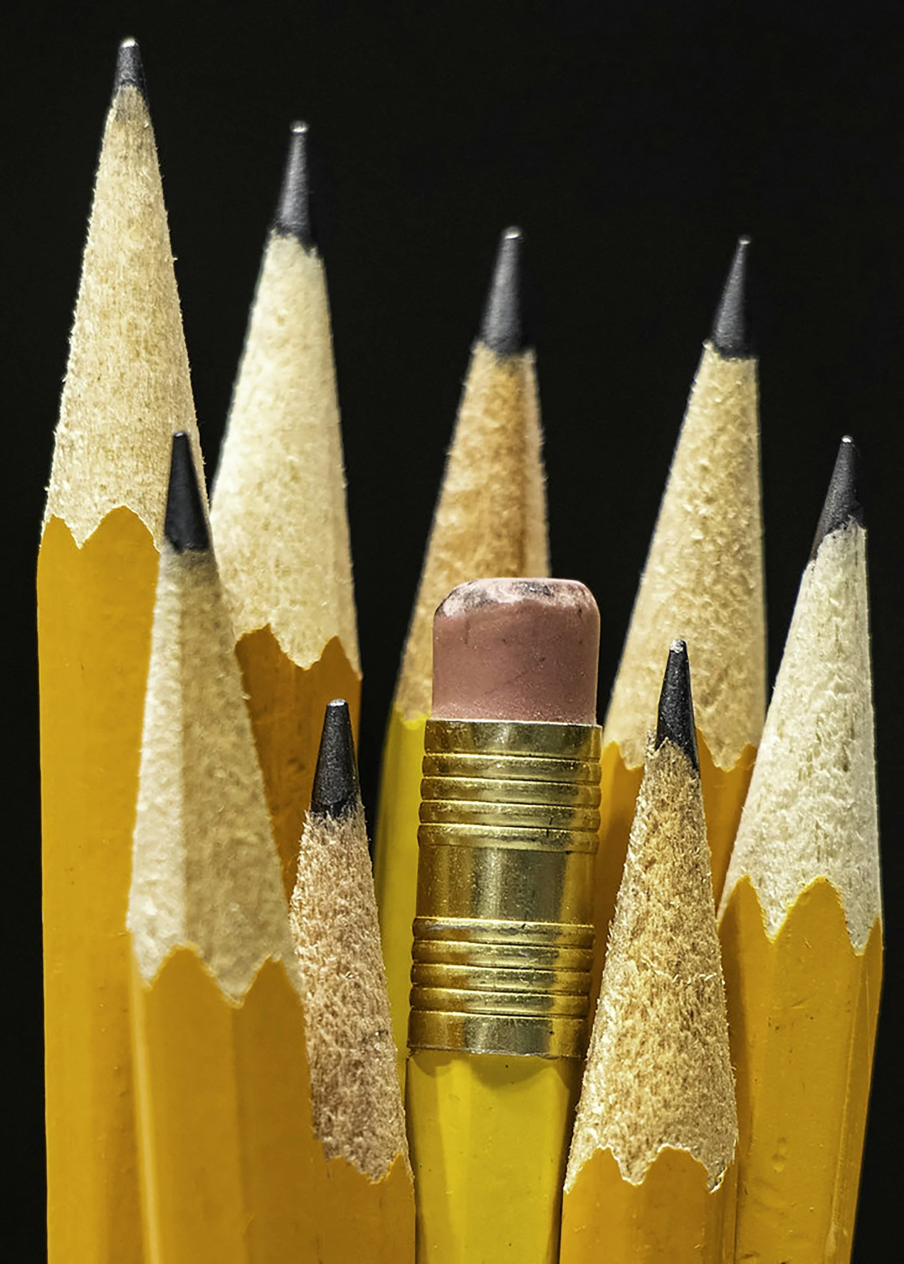 Close-up of yellow pencils with black tips and a pink eraser in the center, arranged vertically against a black background.