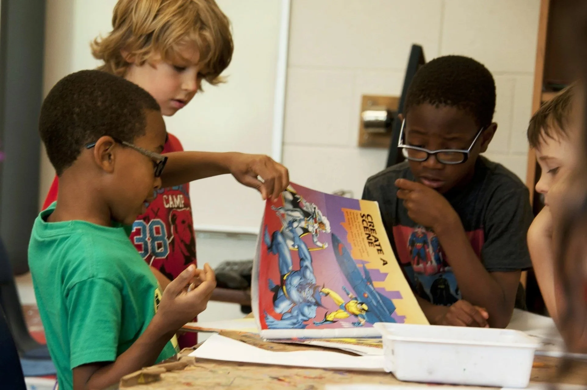 A group of children gathered around a table, looking at a comic book featuring a superhero.