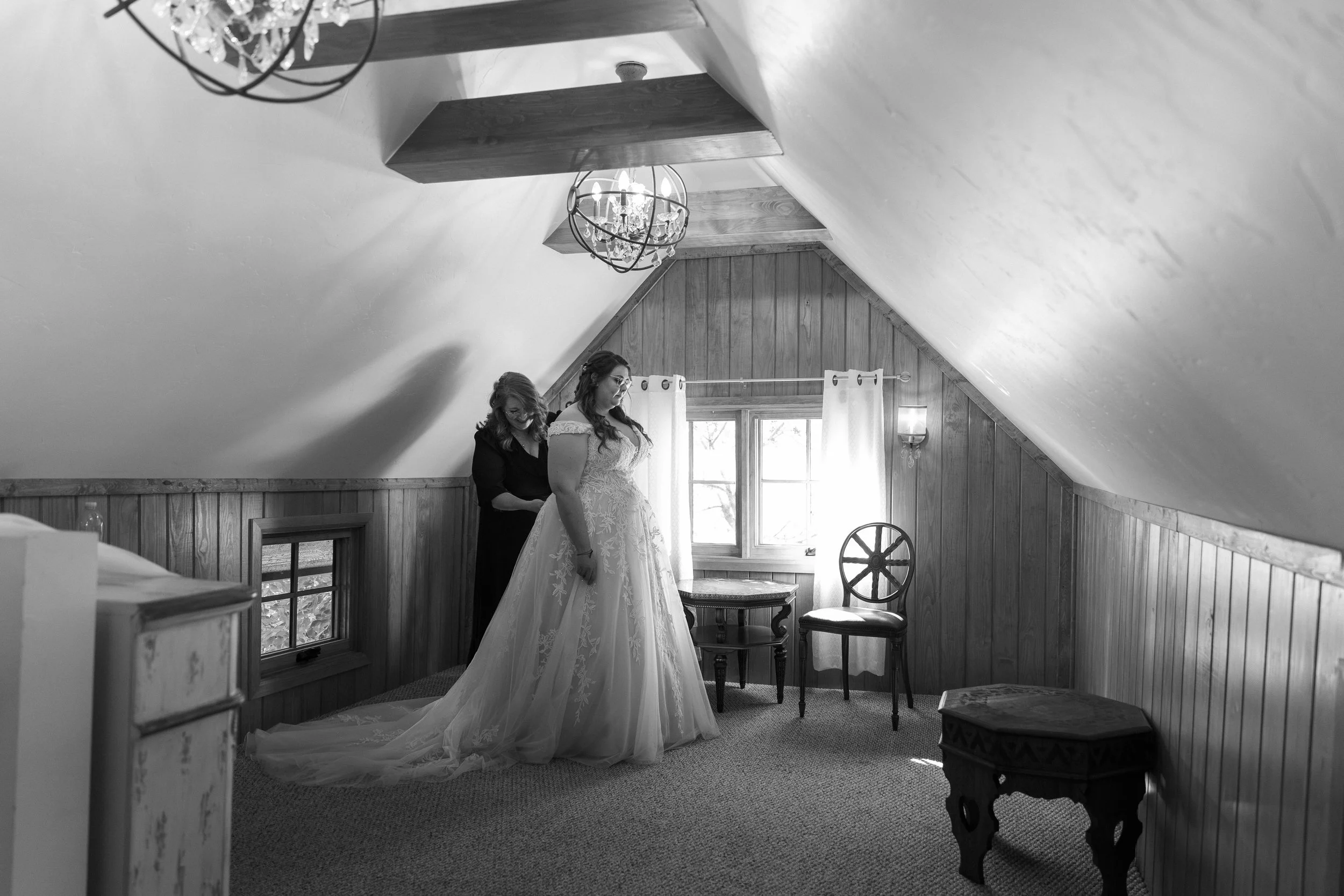The bride's mom helping the bride put on her wedding dress.