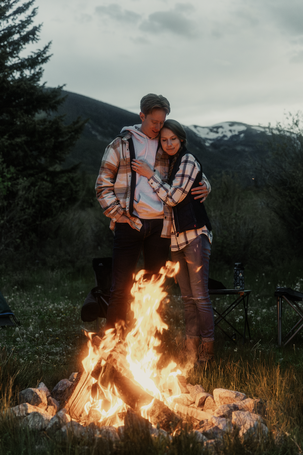 Couple standing closely together next to a fire during camping engagement session in Buena Vista, Colorado.
