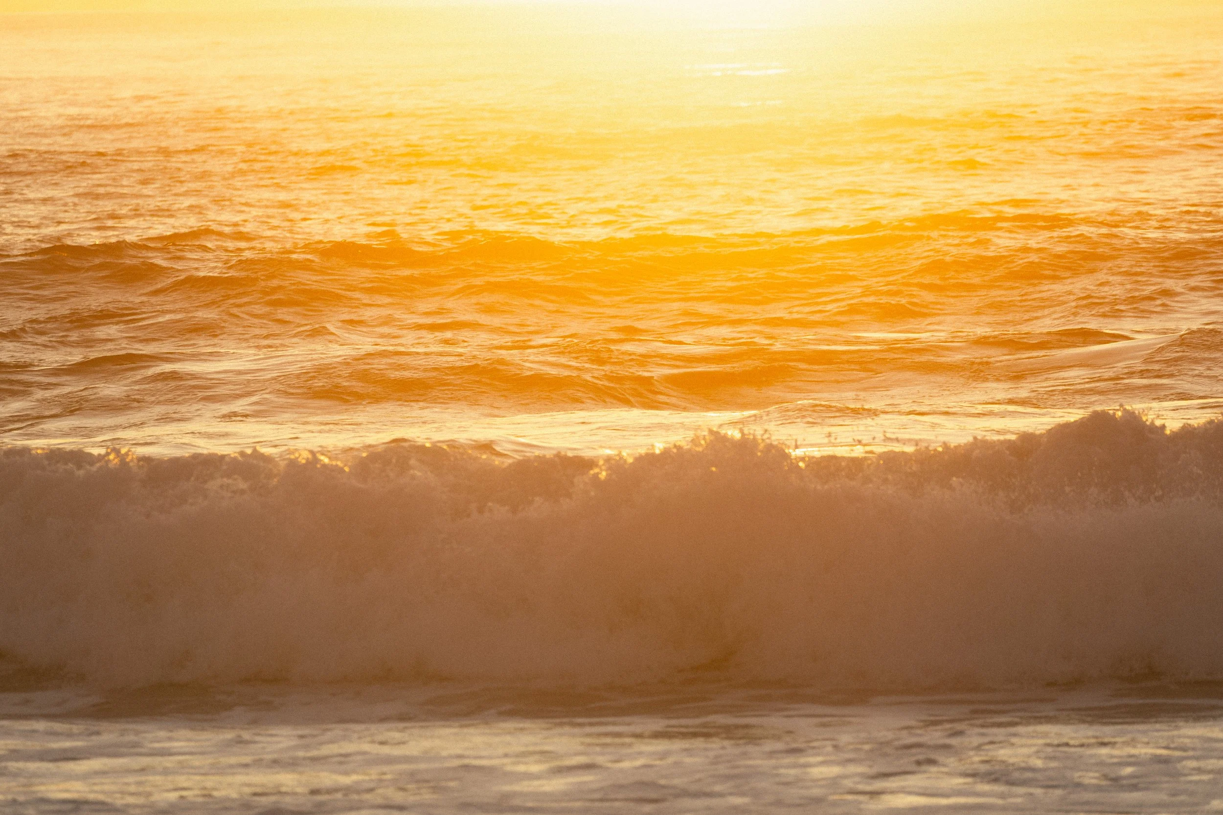 Sunset over the ocean with waves crashing onto the sandy shore.