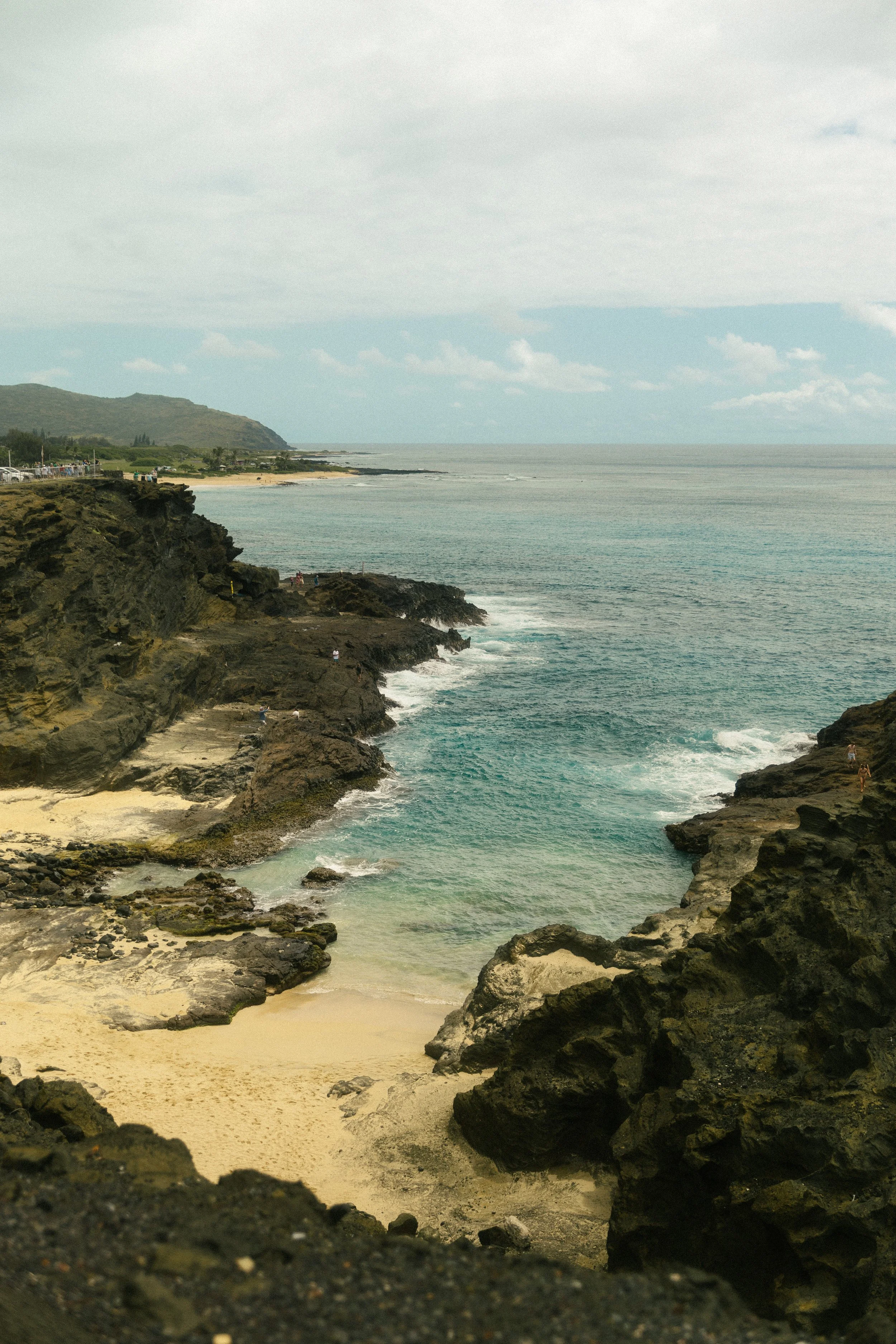 Coastal landscape with rocky cliffs, sandy beach, and ocean under cloudy sky.