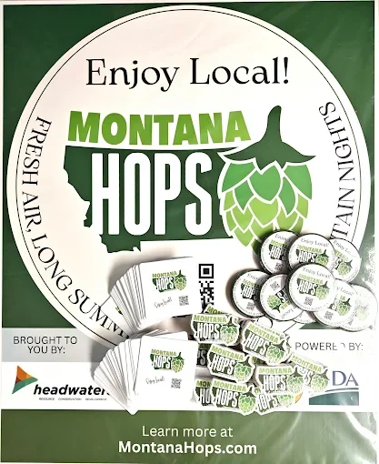 Promotional poster for Montana Hops, featuring a hop cone, stacks of branded items, and text encouraging local, fresh, and sustainable hops. Includes website URL MontanaHops.com.