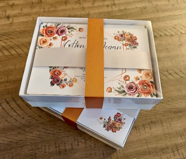 A white gift box with floral patterns and a brown band, placed on a wooden surface.