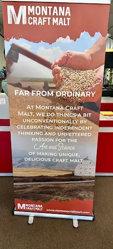 Montana Craft Malt banner featuring a hand holding a hammer over grains with a mountain and sky background, with text about Montana Craft Malt's unique approach and pride in craft malt