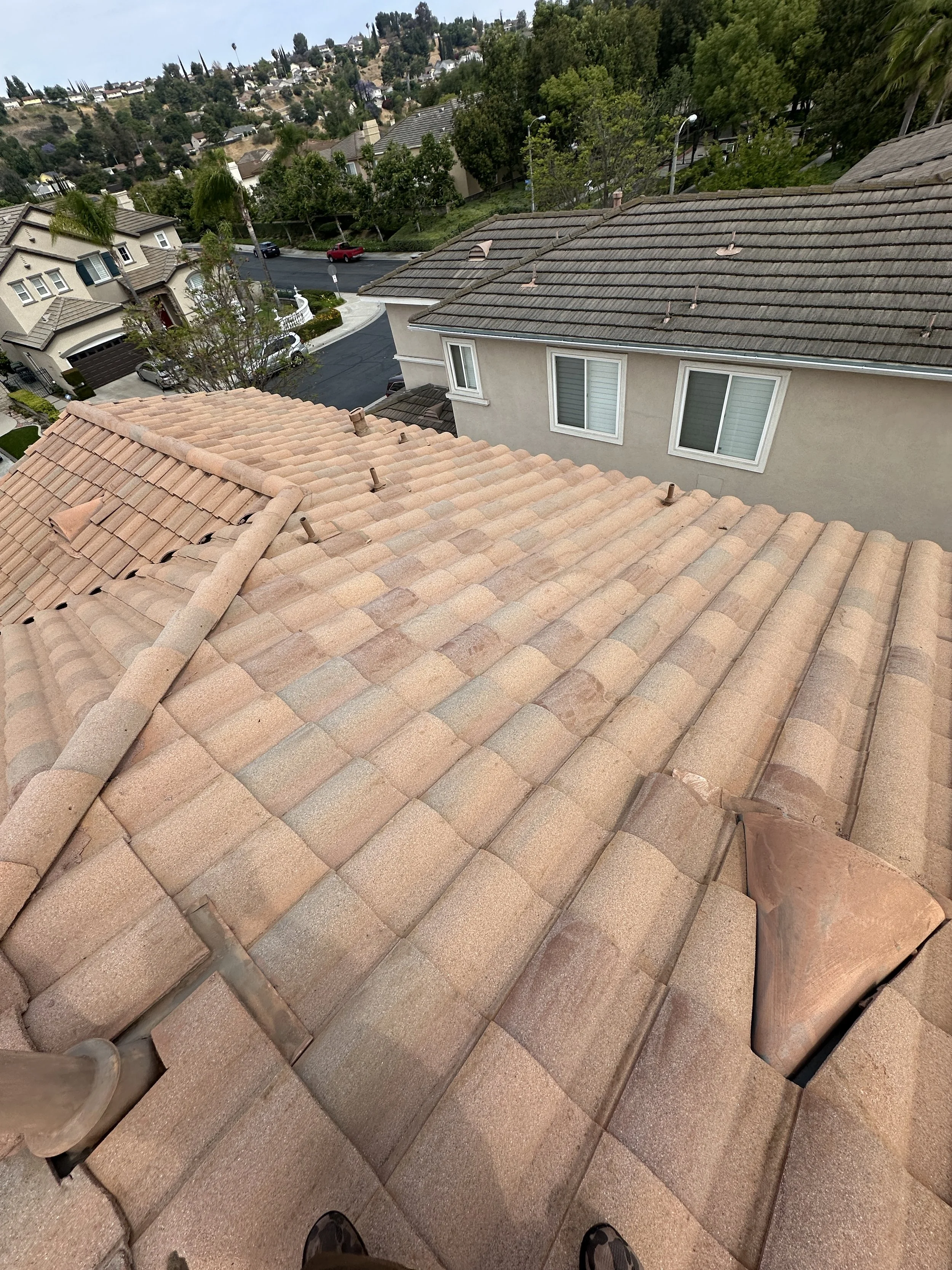 View of a tiled rooftop from above, with neighboring houses, trees, and a street with cars visible in the background.