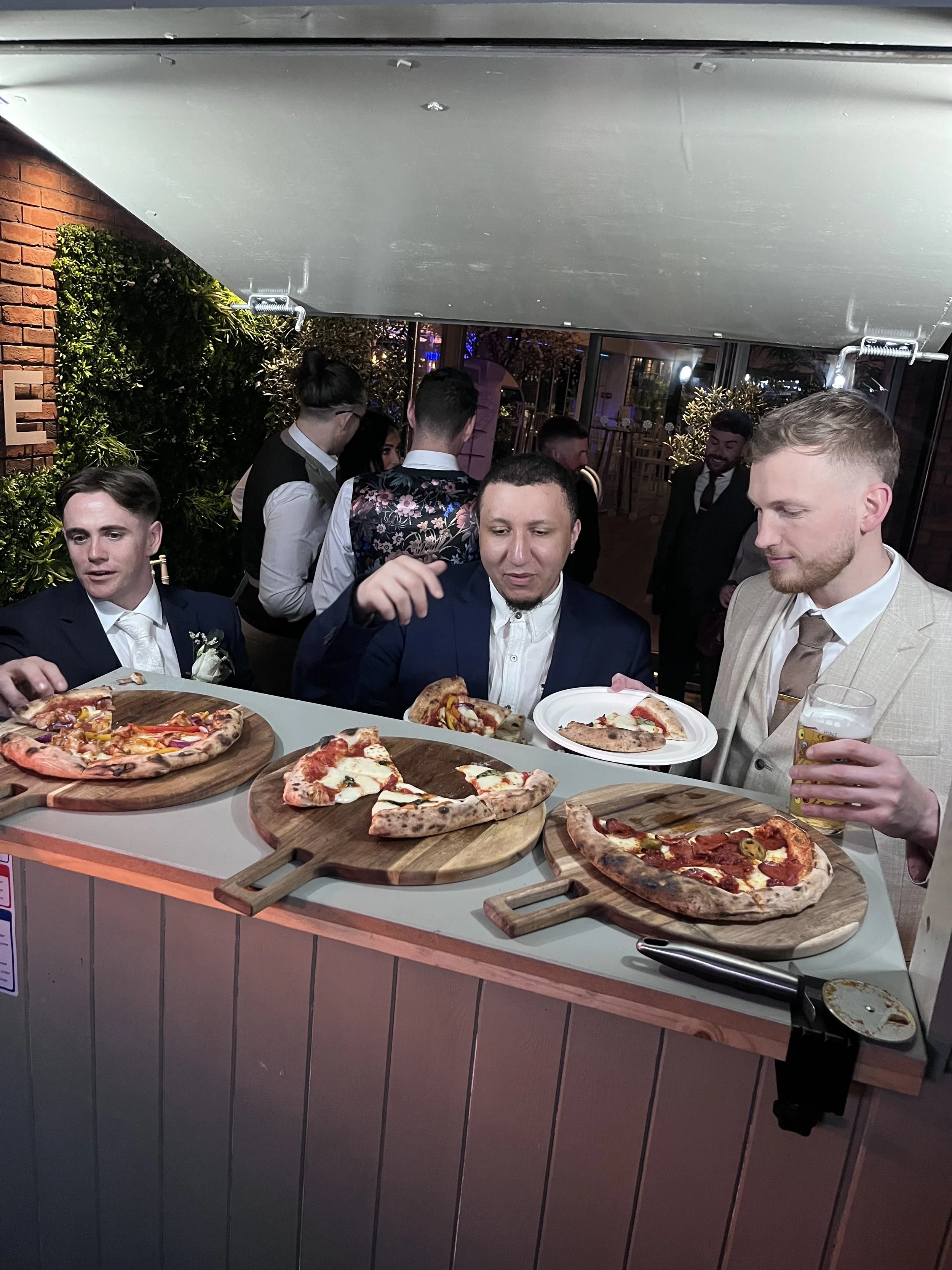 Men and women in formal attire enjoying pizza and drinks at a social gathering or celebration.