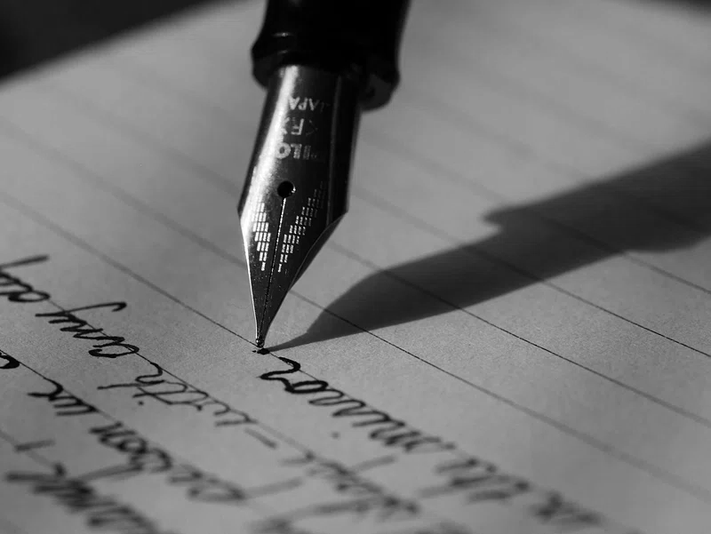 Close-up of a fountain pen writing on lined paper with cursive handwriting in black ink.