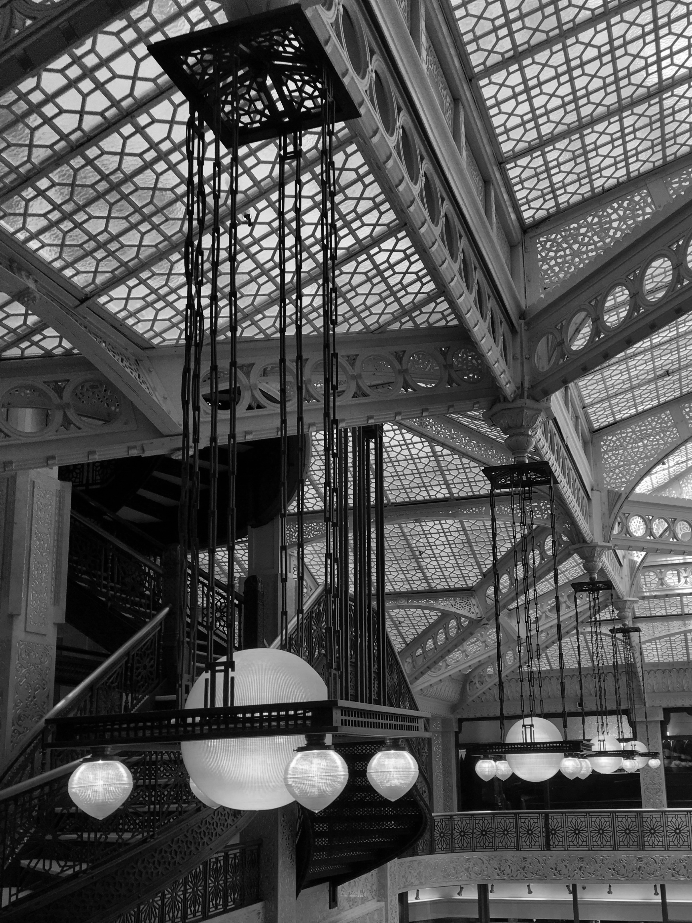 Ornate interior of a building with intricate metalwork on the ceiling, geometric patterns, and hanging spherical pendant lights.