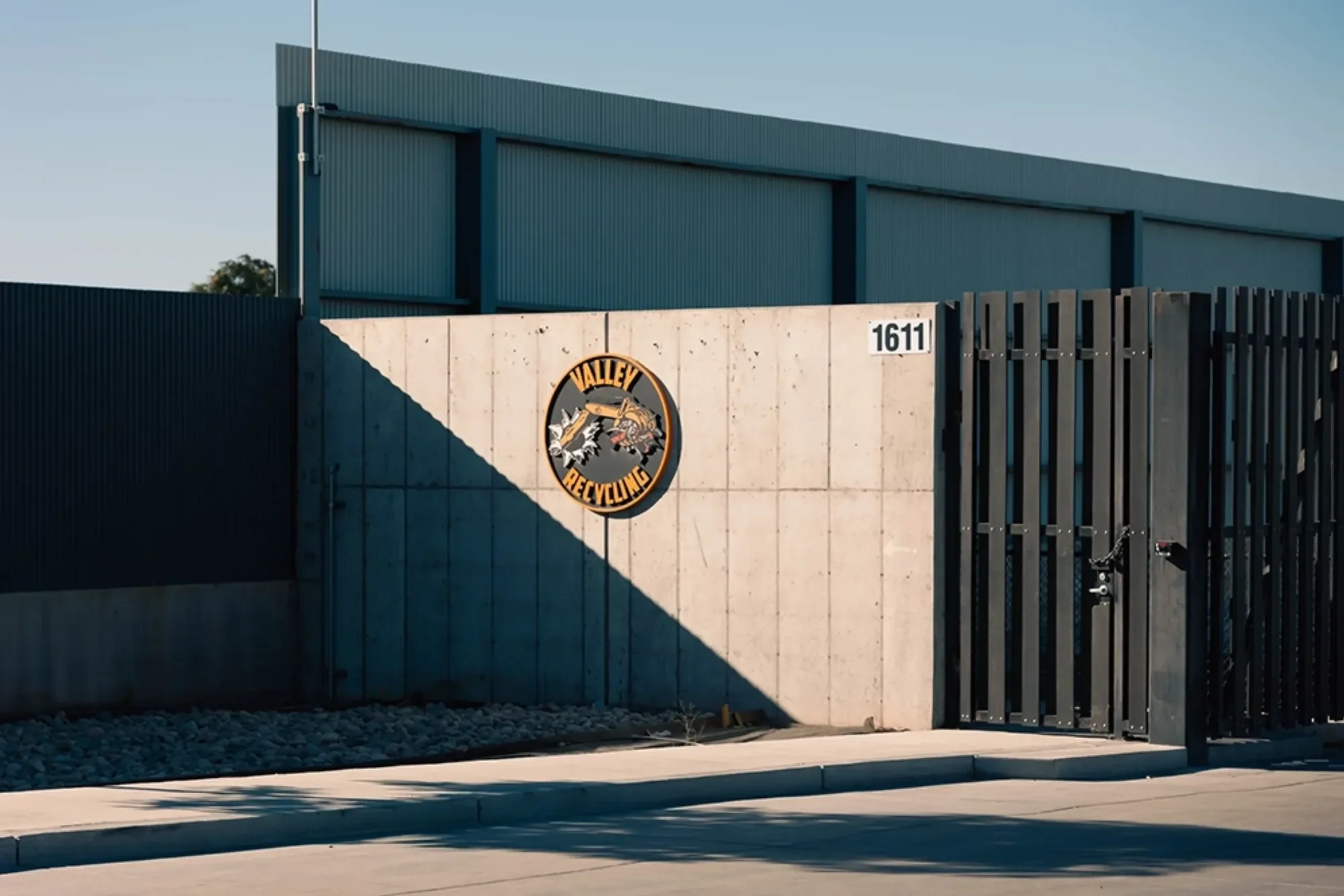 The entrance gate of Valley Recycling, a recycling facility, with a concrete wall displaying the Valley Recycling logo and the street number 1611. Located in an industrial area with a blue building behind the wall.