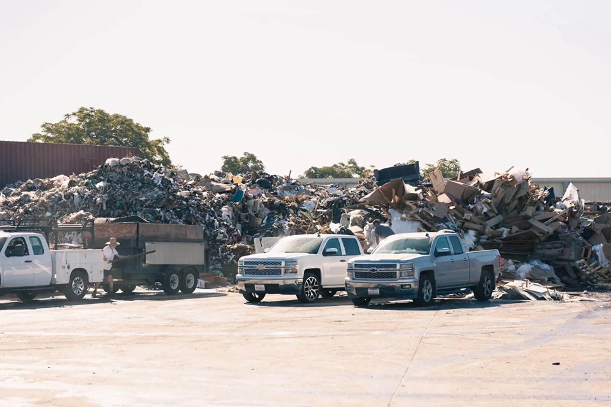 Pile of garbage with several trucks at a landfill site, clear sky in the background.