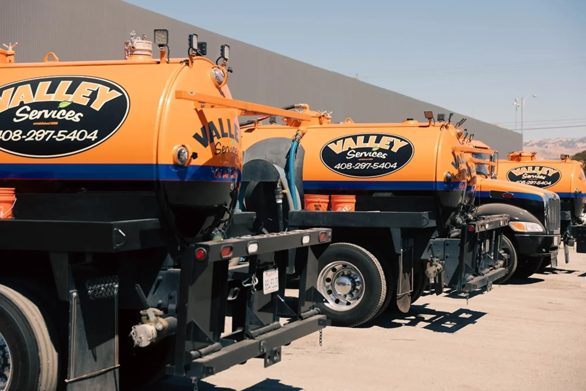 Multiple orange Valley Services trucks with black and blue stripes parked in a lot.