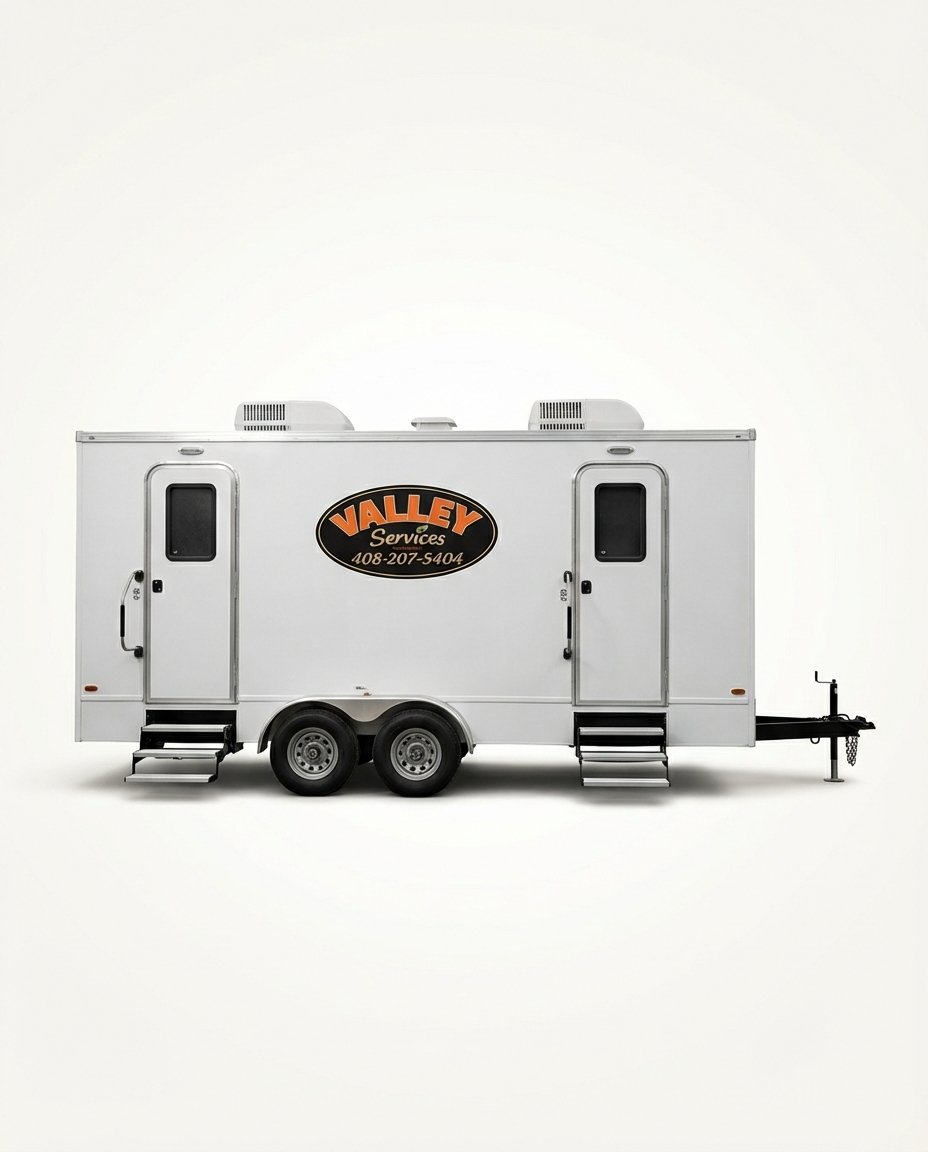 White mobile service trailer with black and orange logo that reads 'Valley Services' and contact number, with external steps leading to doors on each side, and two air conditioning units on the roof, set against a plain white background.