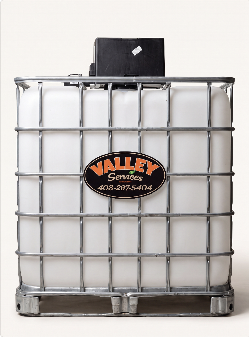 Large white plastic IBC container with metal cage, labeled "Valley Service."