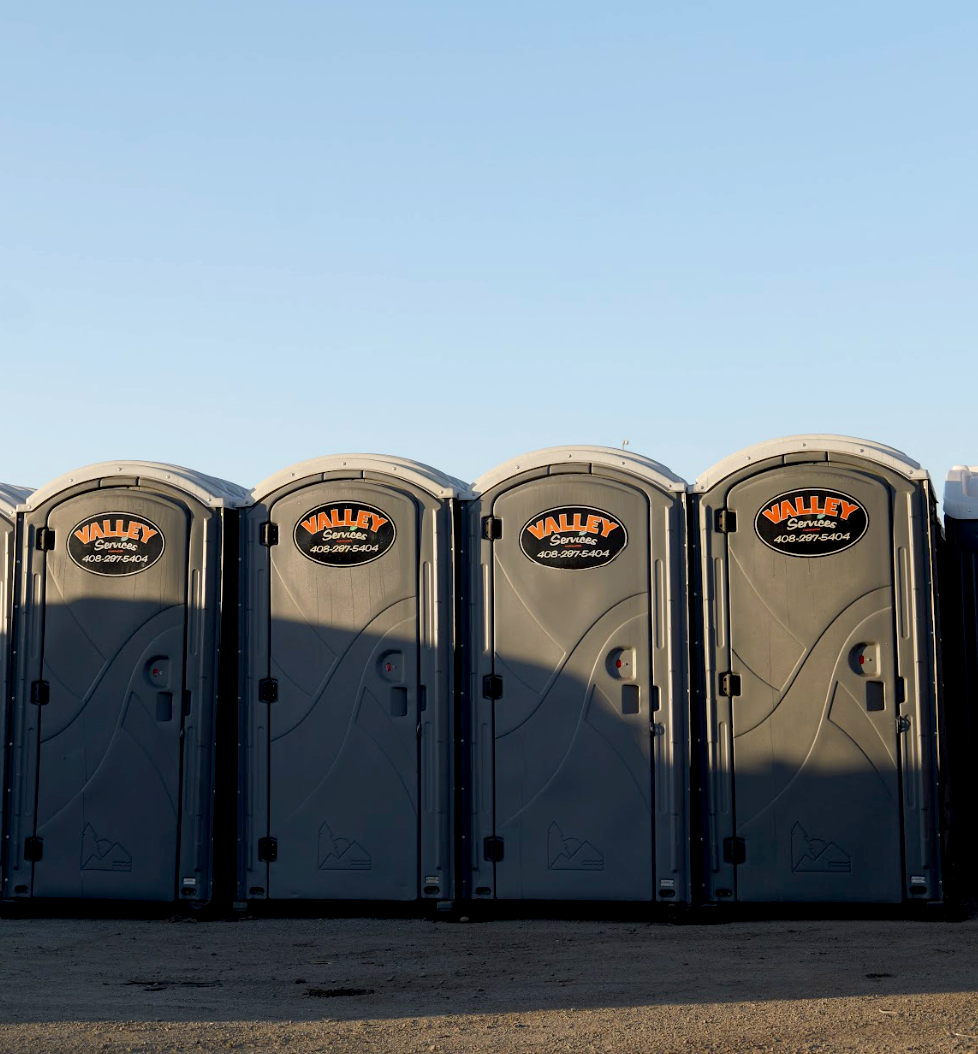 A row of portable toilets with a clear blue sky background.