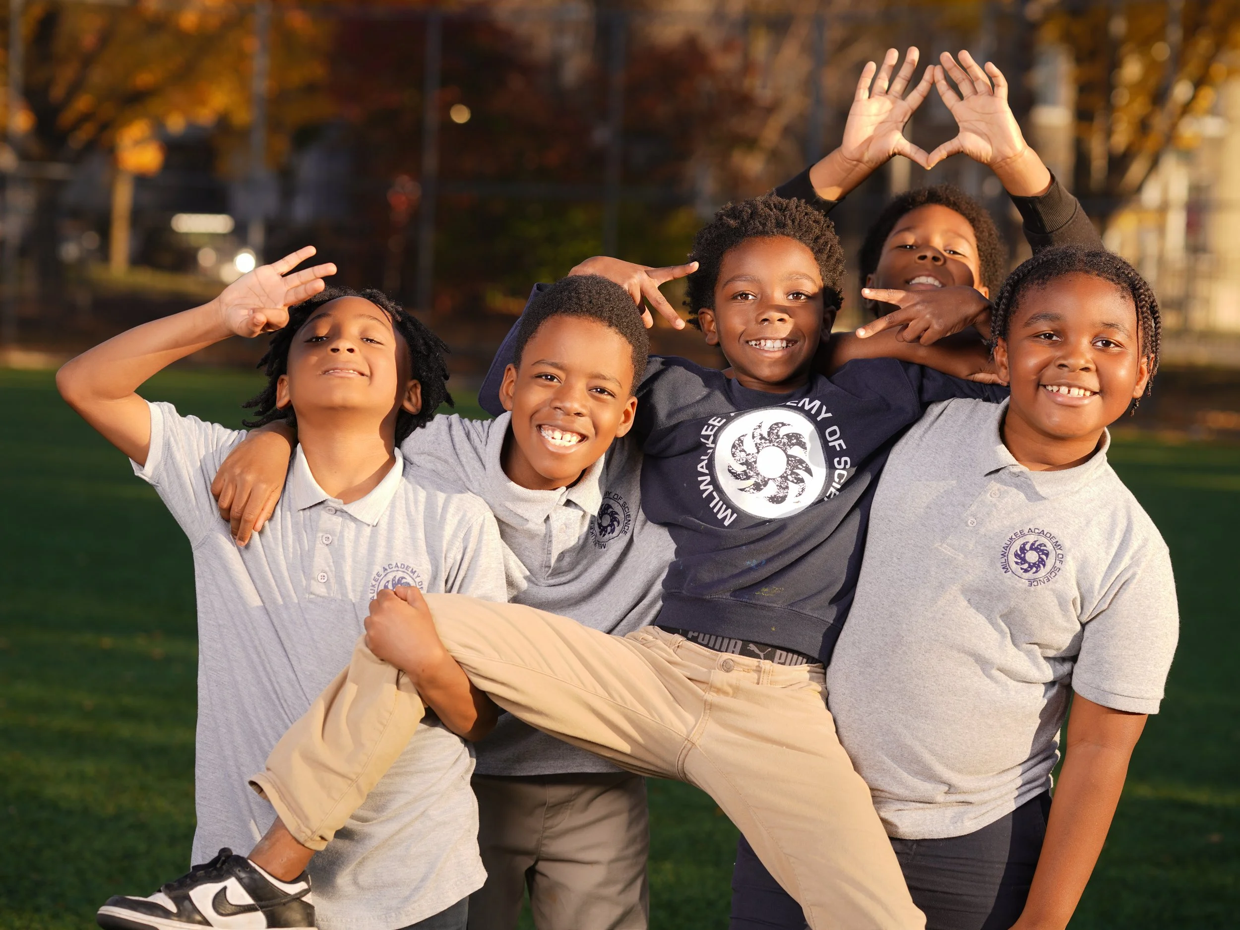 Group of four smiling children with curly hair, wearing casual clothes, making gestures, and having fun outdoors in a park during autumn.