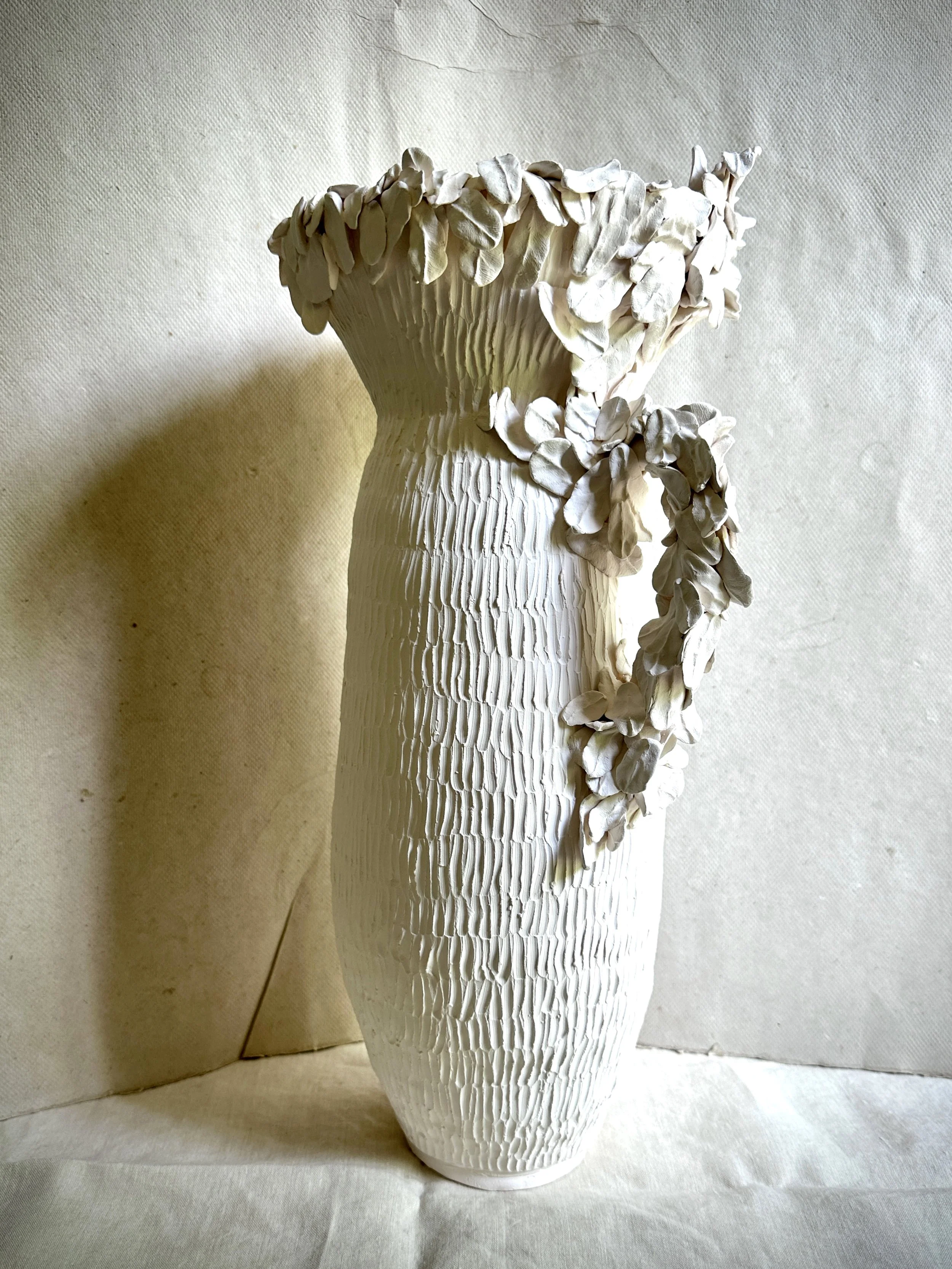 Decorative white ceramic vase with textured surface and leaf-like embellishments on top.
