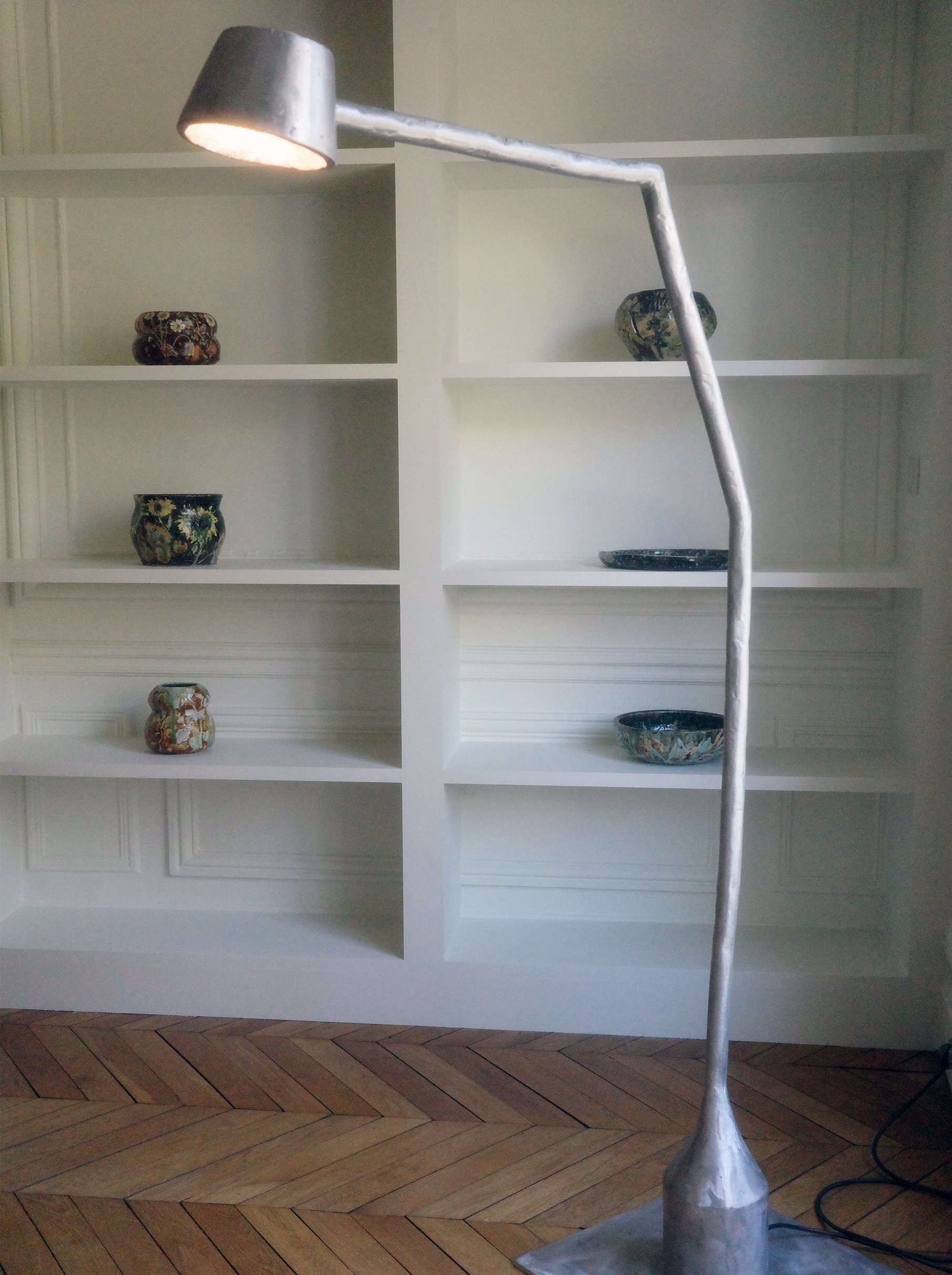 Two metal floor lamps with adjustable arms and cylinder-shaped shades, standing on a wood floor with a fabric backdrop.