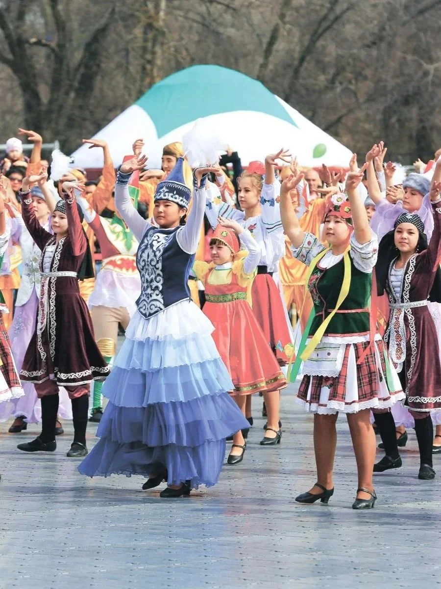 Children performing a traditional dance in colorful folk costumes outdoors with a tent in the background.