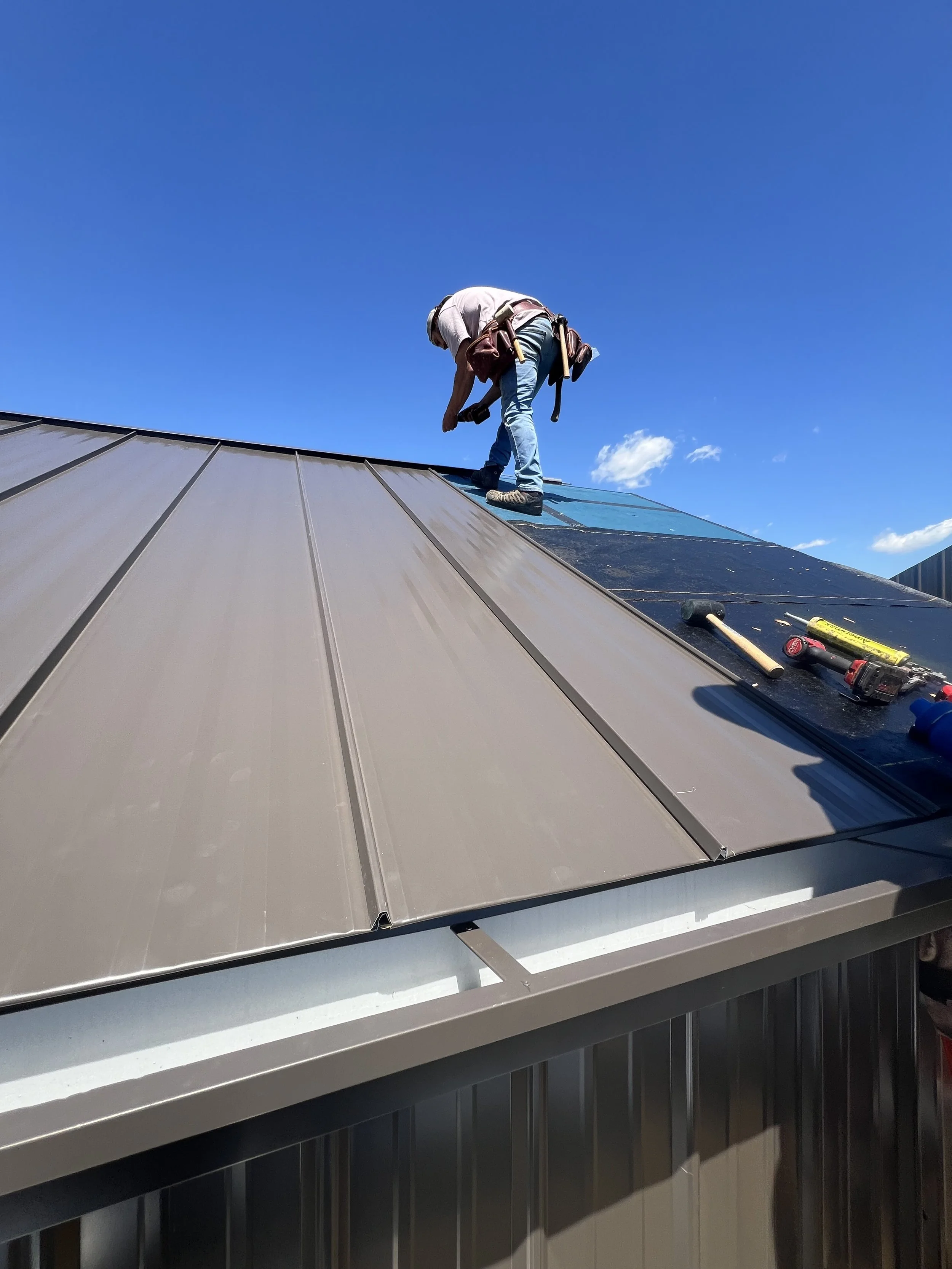 Worker on metal roof installing or repairing roofing panels with tools on a sunny day