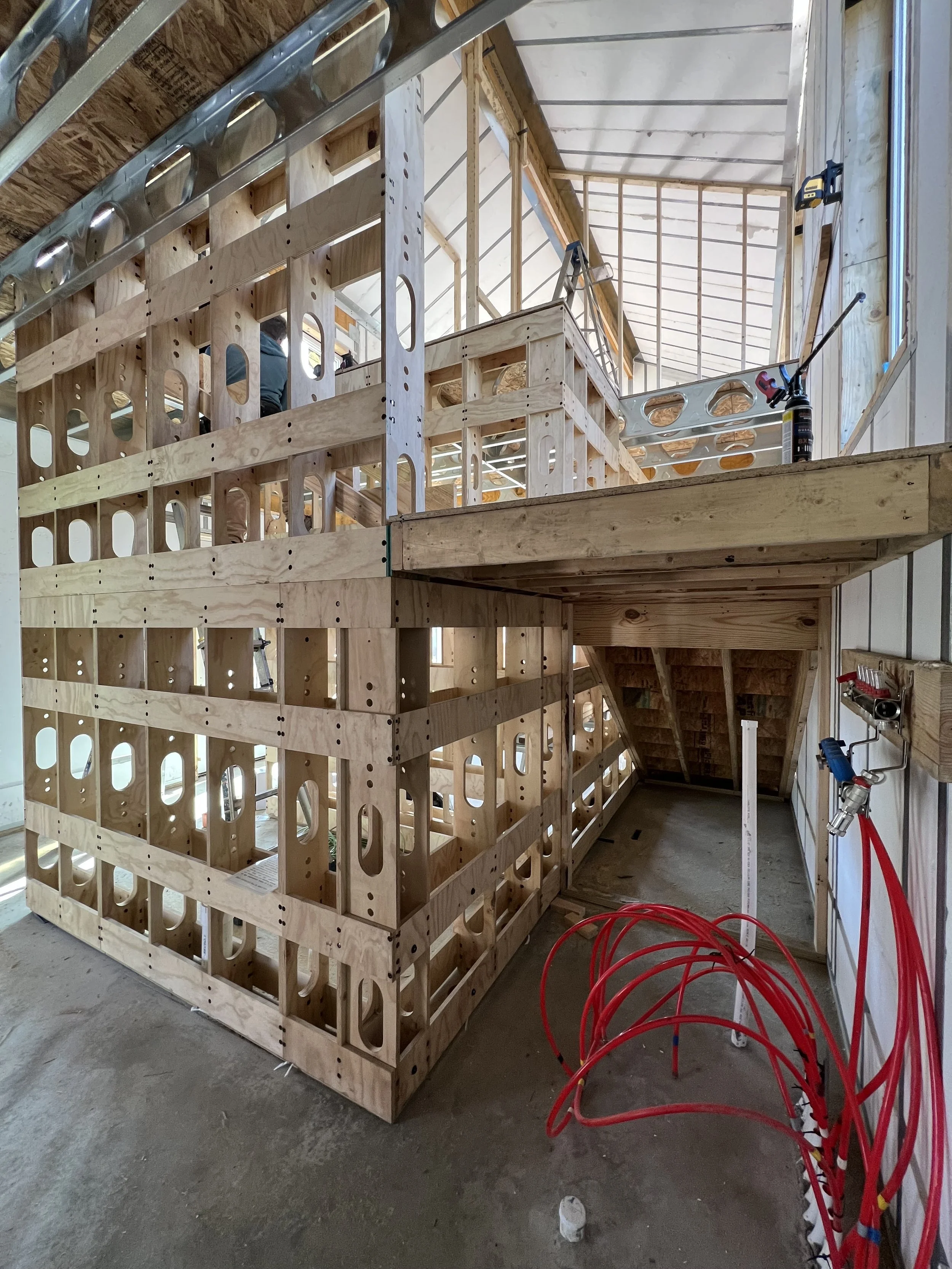 Construction of a wooden staircase with framing in progress inside a house under construction, with tools and red hoses nearby.