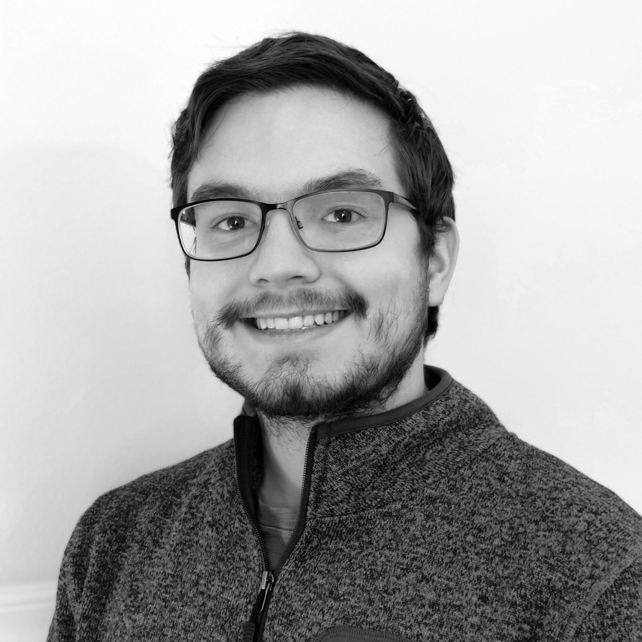 Black and white portrait of a smiling young man with glasses, wearing a zip-up sweater, against a plain background.