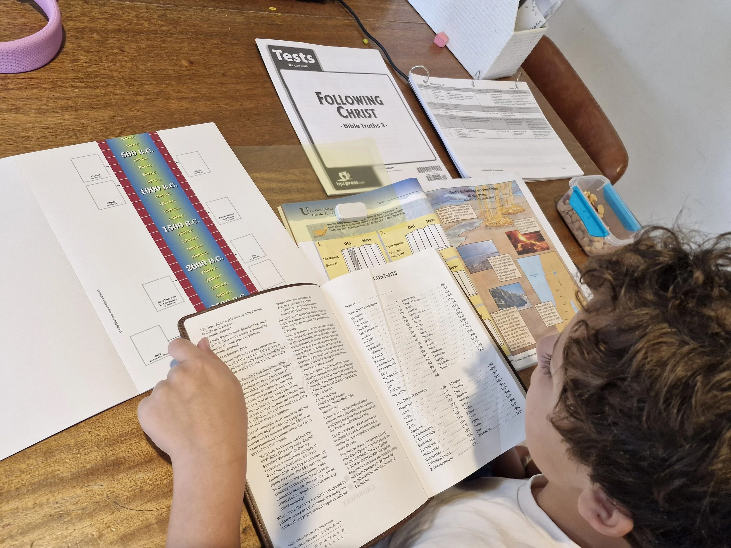 Luke doing BJU Press Homeschool Bible 3 with the workbook, tests, and more open.