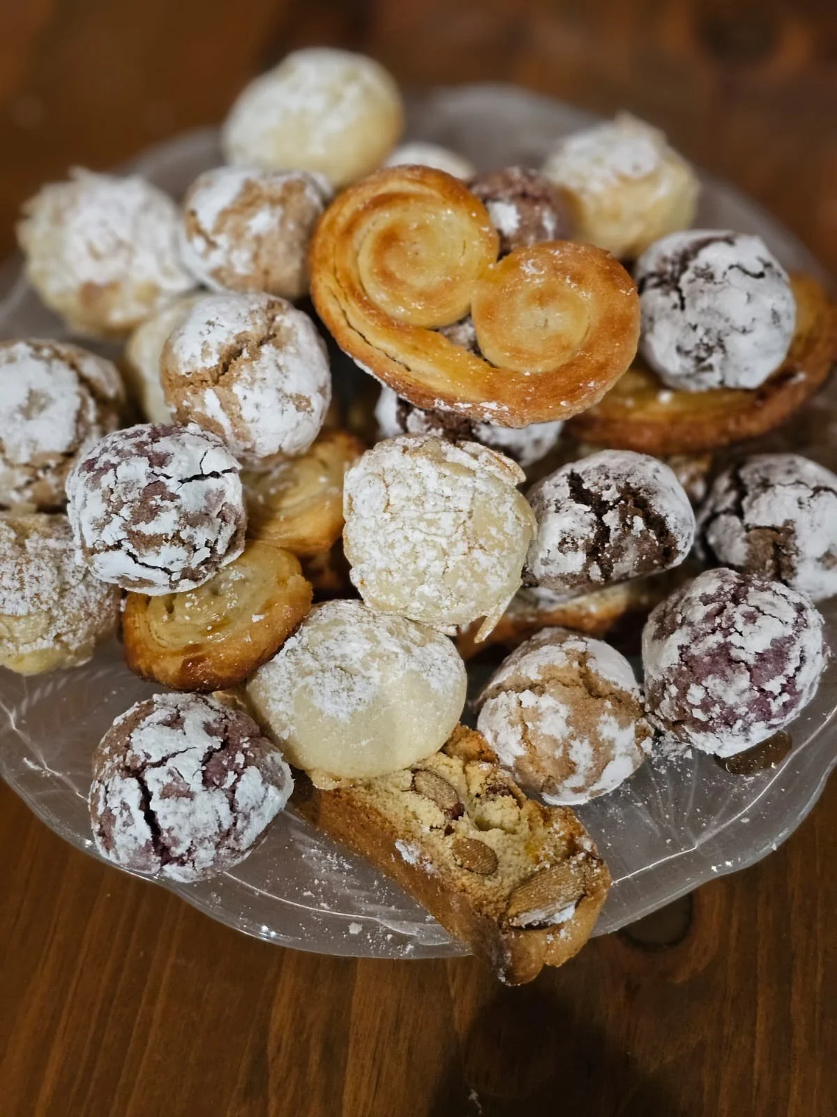 Assorted cookies and pastries dusted with powdered sugar on a glass plate.