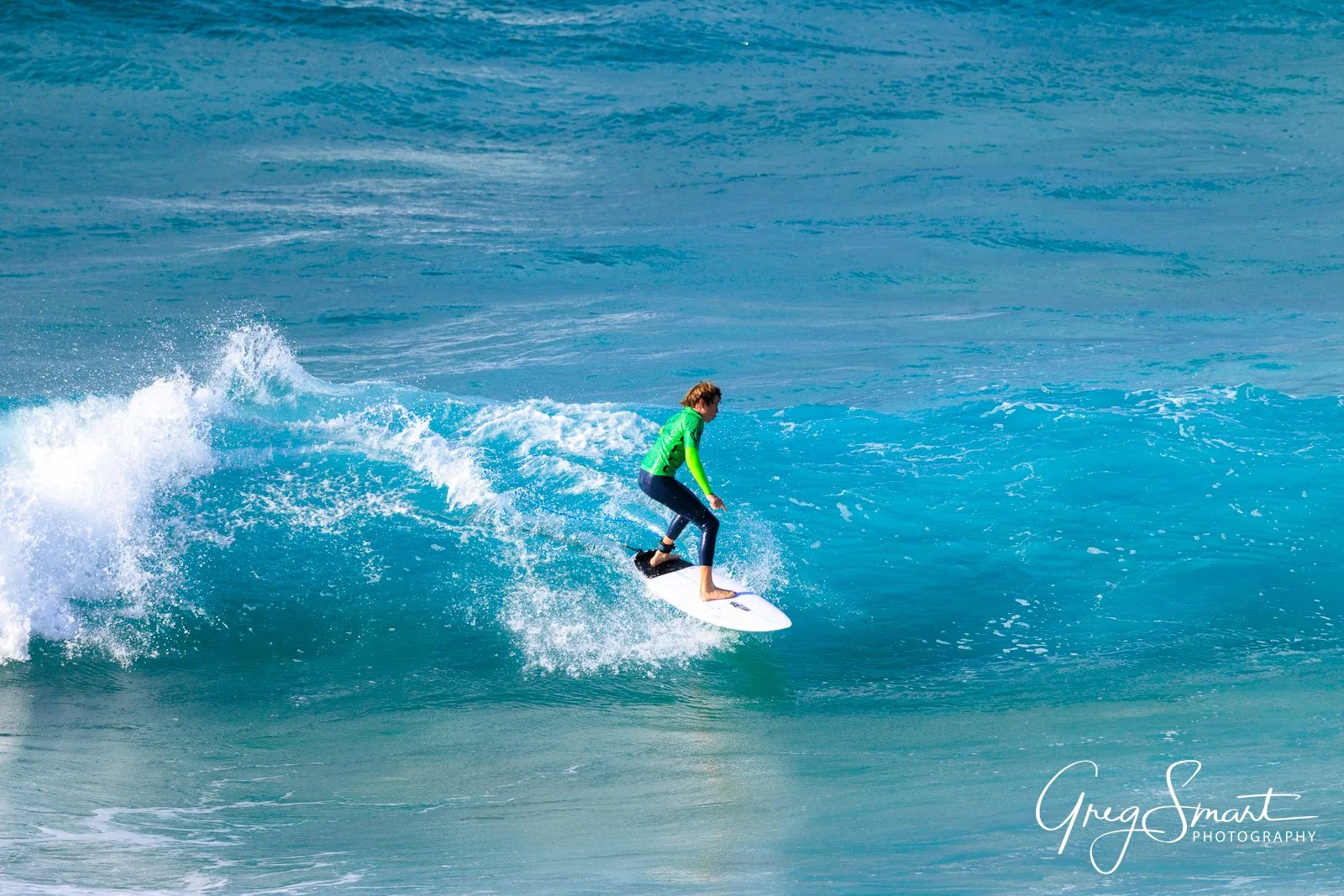 Person surfing on a wave in the ocean, wearing a green and blue wetsuit.