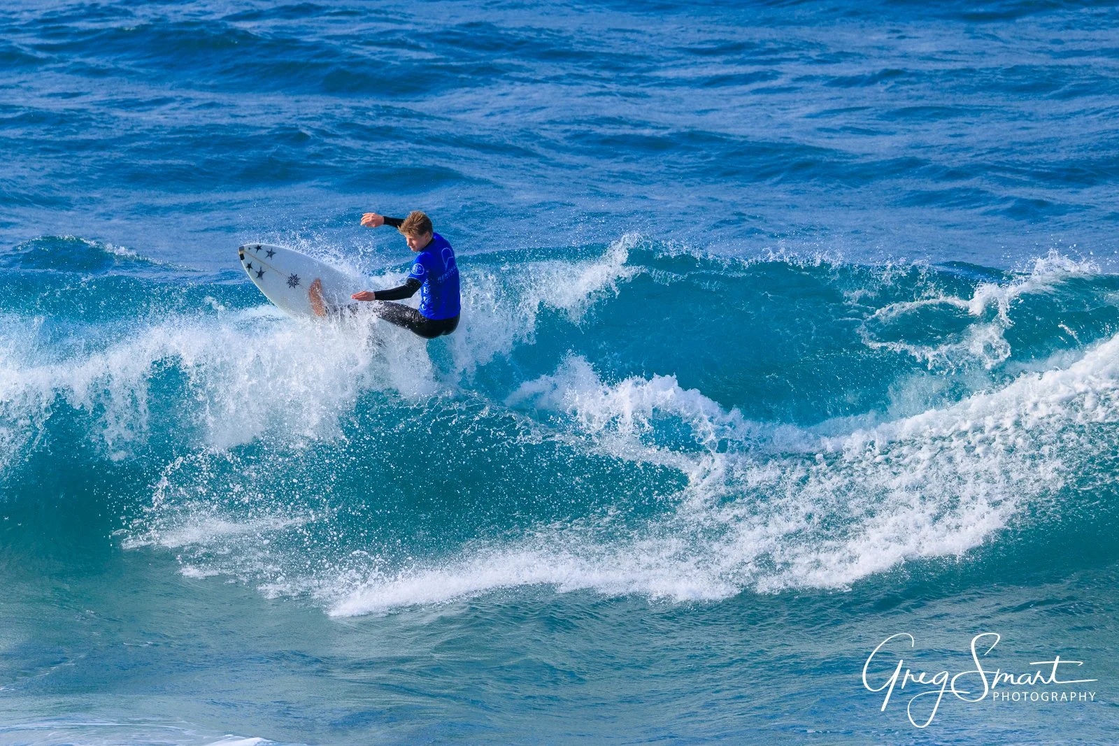 A surfer in a blue shirt riding a wave in the ocean.