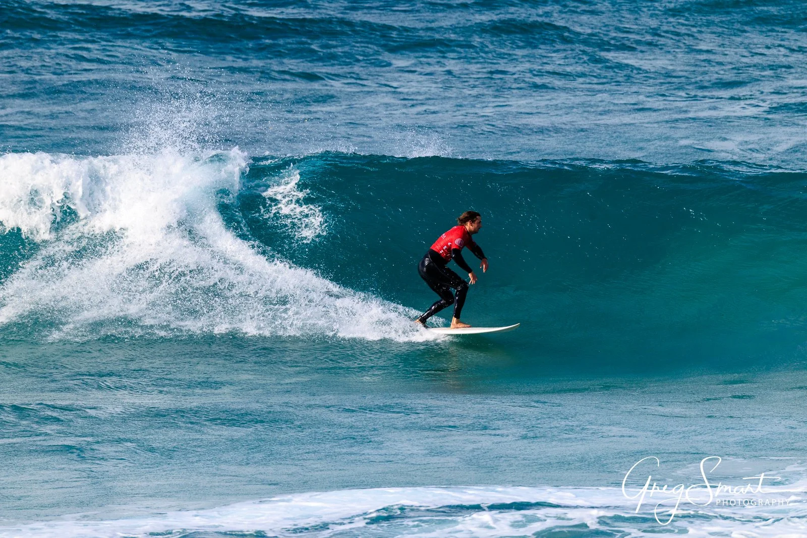 A person in a red shirt surfing on a wave at the beach.