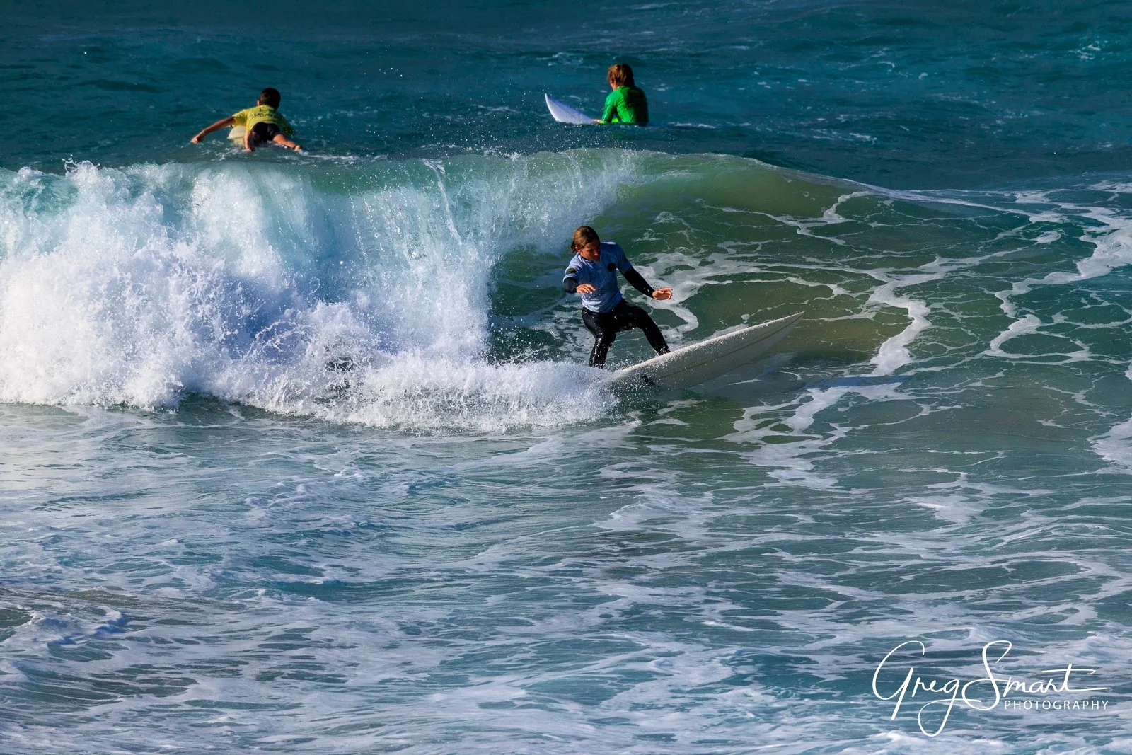 Surfer riding a wave with two other surfers and a person on a paddleboard in the background.