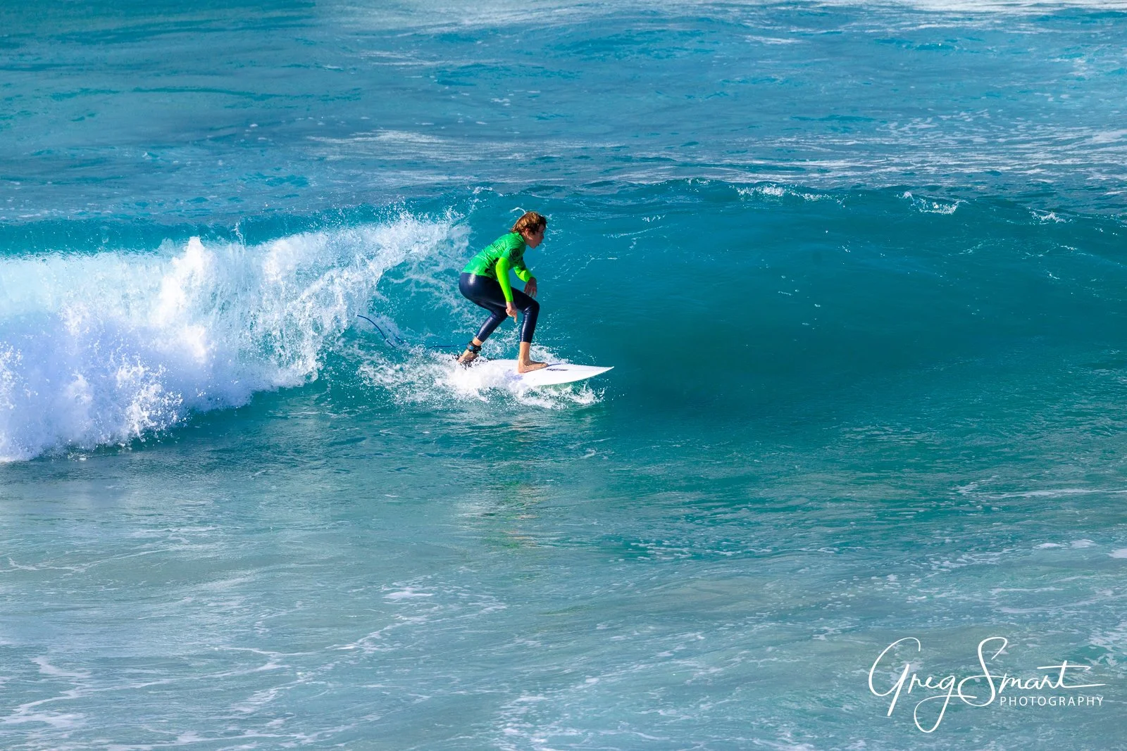 A woman in a bright green wetsuit surfing on a small wave in the ocean during daytime.