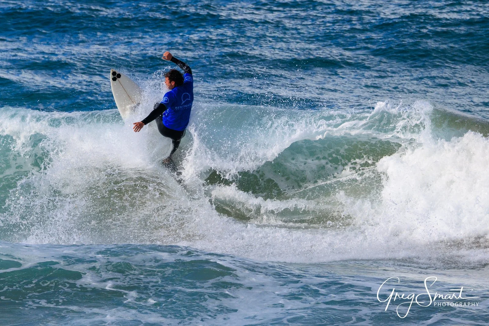 A person in a blue shirt surfing on a wave in the ocean.