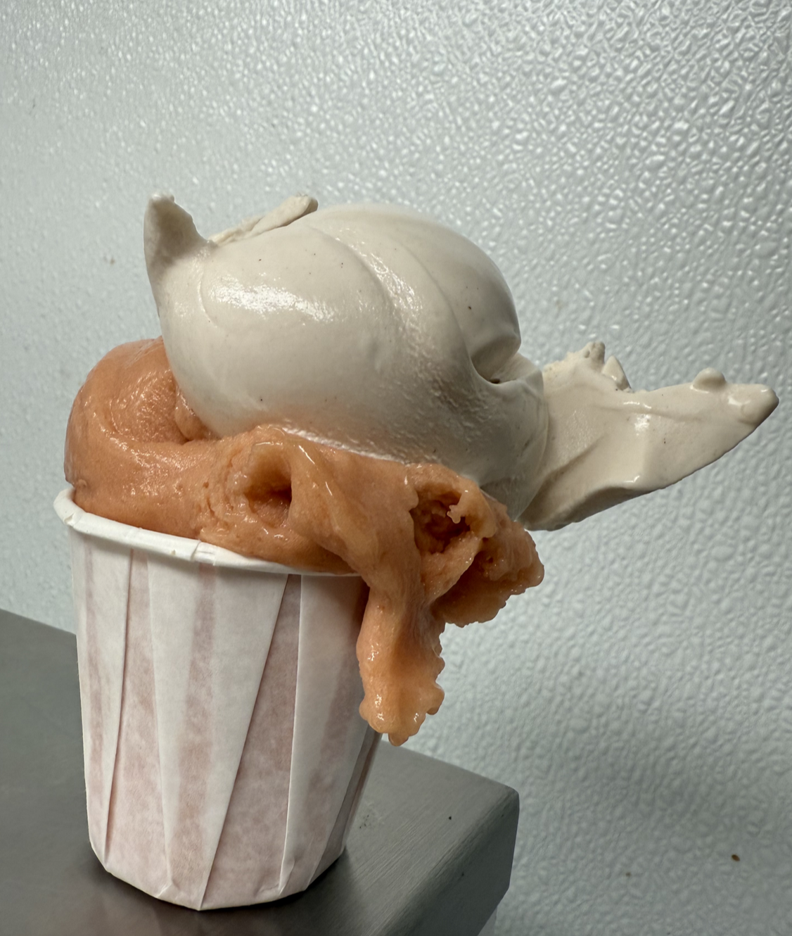 A cup of frozen yogurt with two flavors, sitting on a gray surface with a textured gray wall in the background.