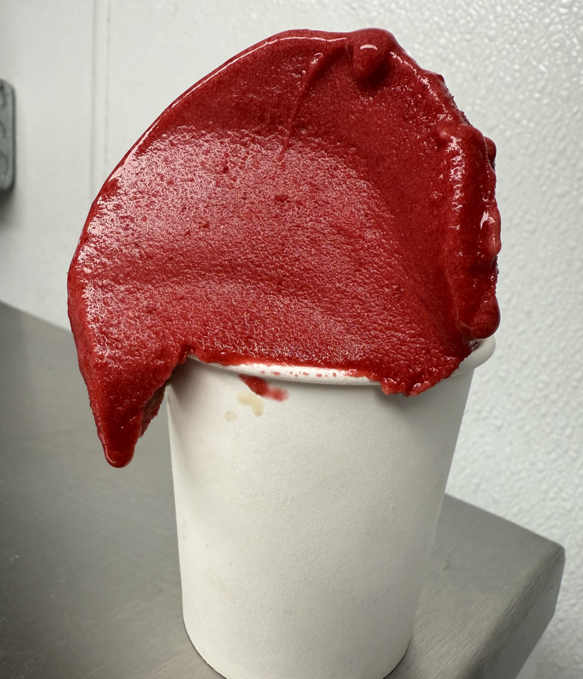 A cup of soft-serve ice cream with a red, fruit-flavored topping dripping over the sides.