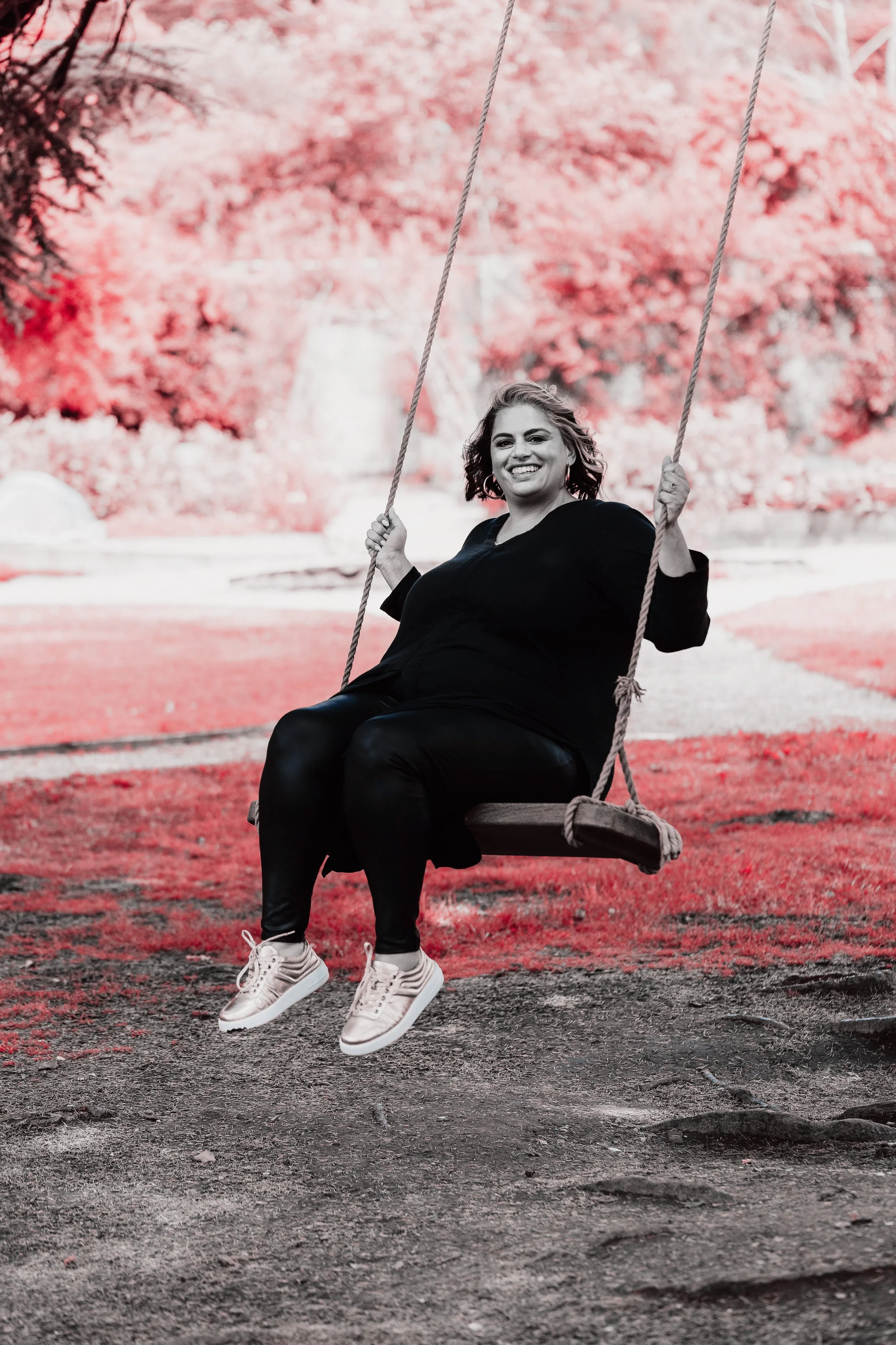A woman smiling while sitting on a swing in a park with pink trees in the background.