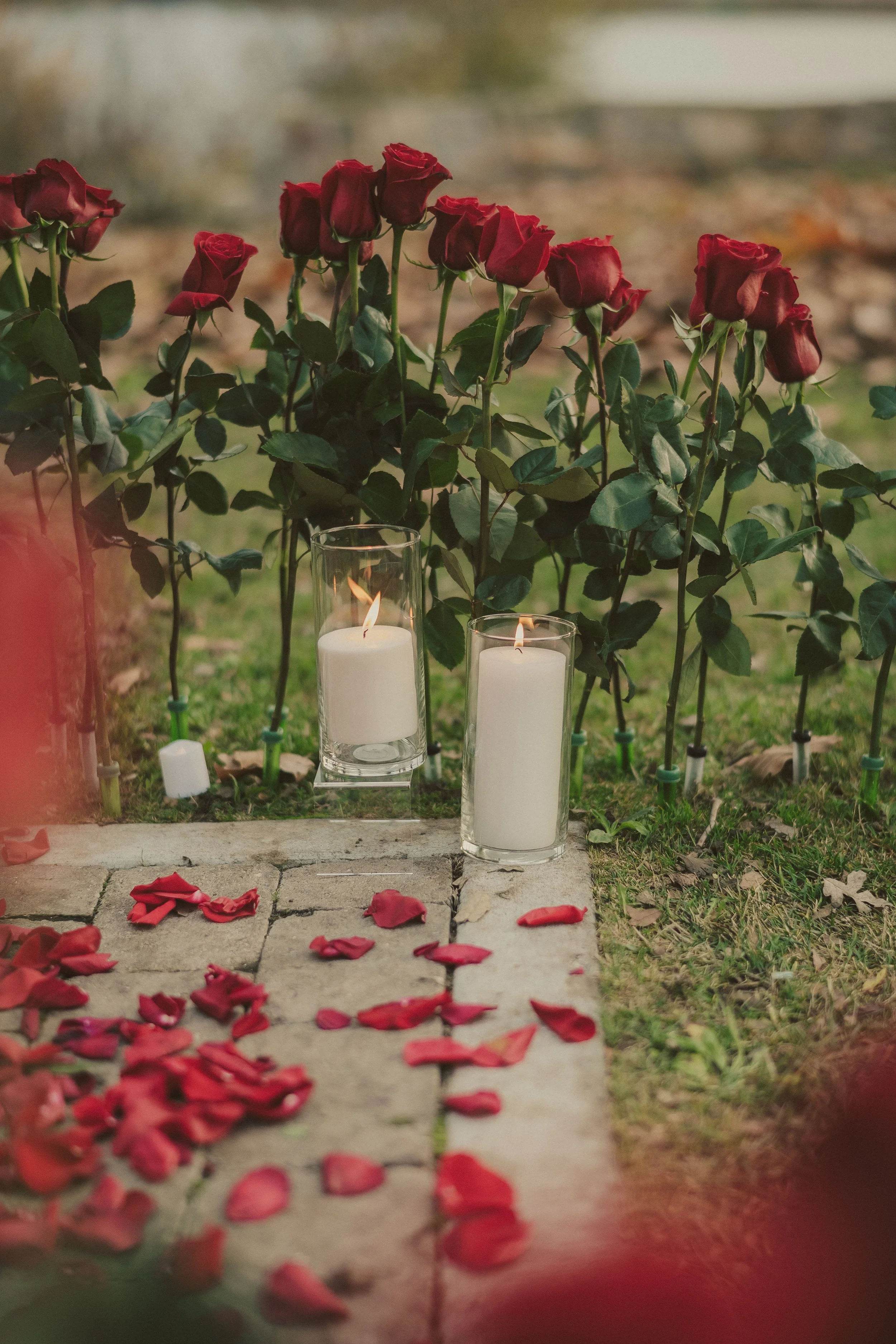 A memorial site with red roses, candles, and rose petals on a stone pathway.
