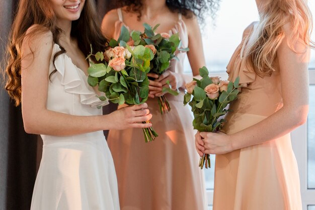 Three women in formal dresses holding bouquets of flowers.