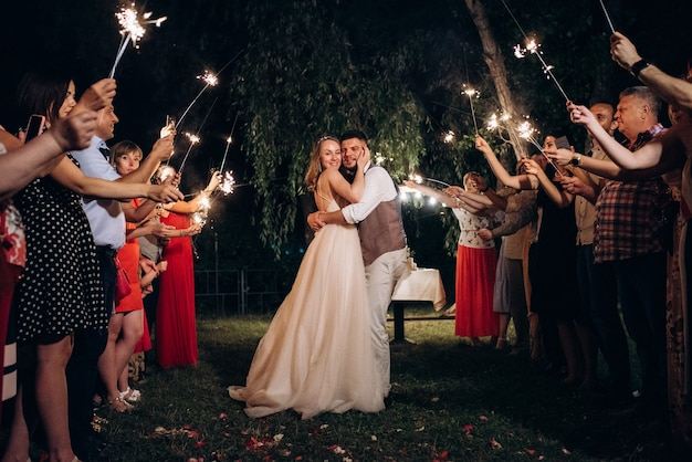 A bride and groom hugging each other at their wedding reception while surrounded by friends and family holding sparklers.